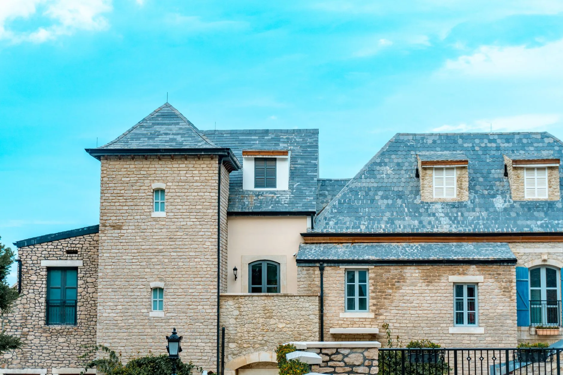 Stone house with a blue grey slate roof, dormer windows and blue shutters under a clear sky