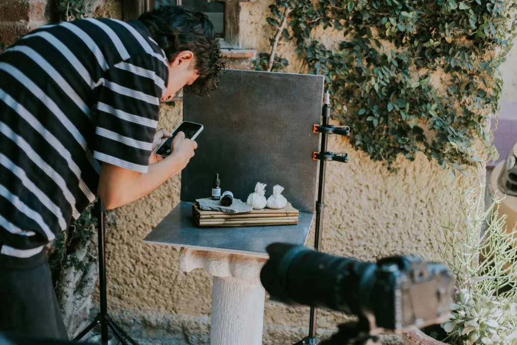 Photographer shooting a small tabletop setup with a phone, with a camera on a tripod beside it