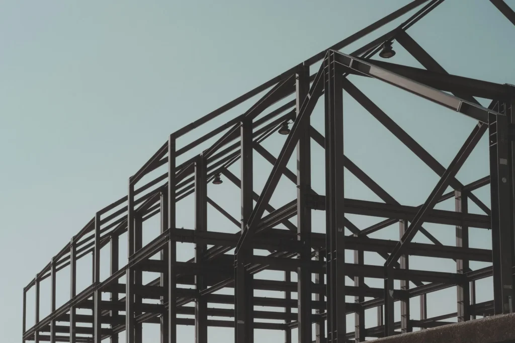 Bare black steel frame of columns, beams and diagonal bracing against a pale sky