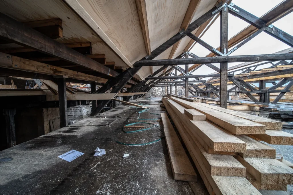 Timber roof beams and steel trusses inside a building under construction with stacked lumber