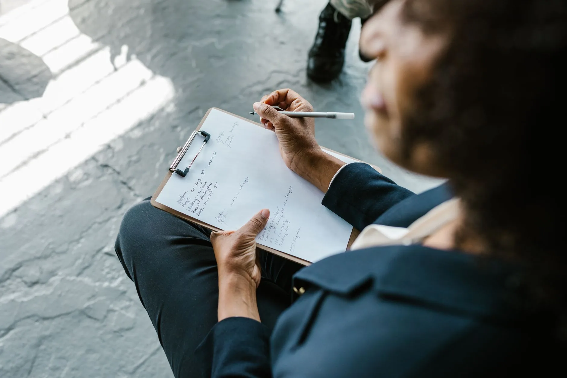 Close view of a person writing handwritten notes on a clipboard held on their lap