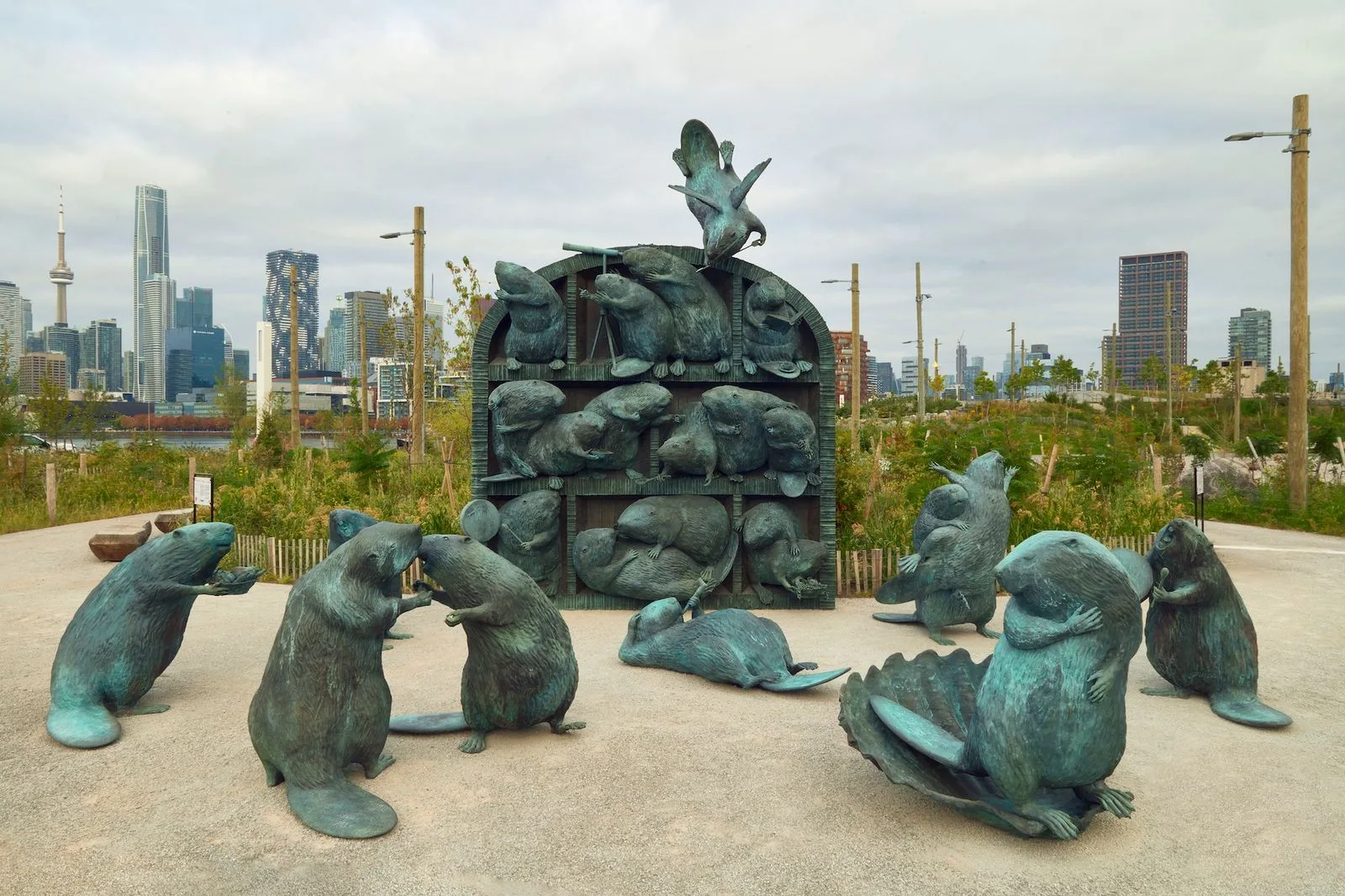 Arched bronze structure filled with beavers, surrounded by large bronze beavers on a paved plaza in a new park