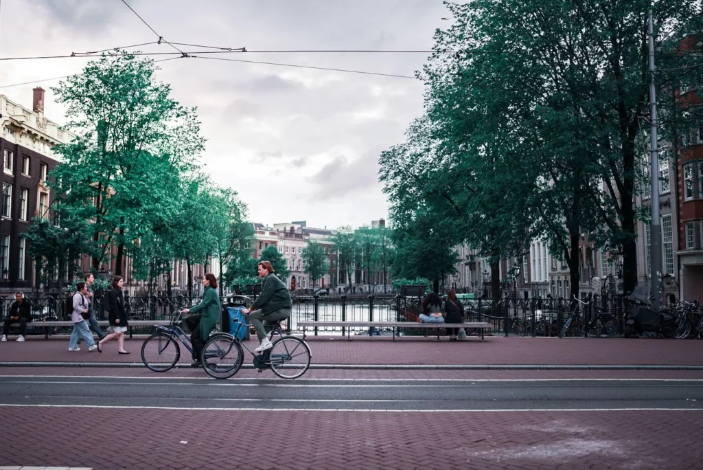 Cyclists and pedestrians sharing a tree-lined street beside a canal in Amsterdam