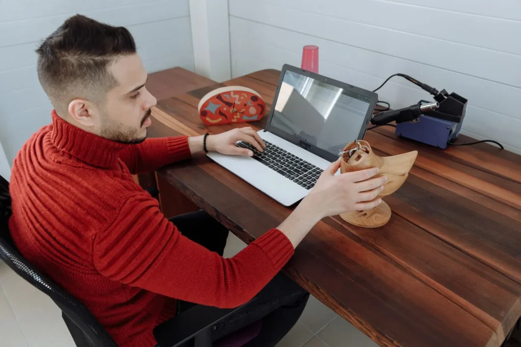Designer modelling on a laptop while holding a carved wooden object for reference