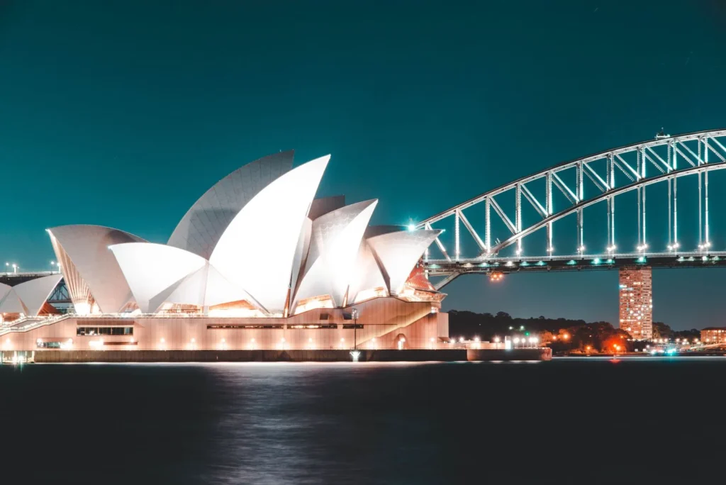 Sydney Opera House shells lit at night with the Harbour Bridge arch behind, one of the world's most iconic city views