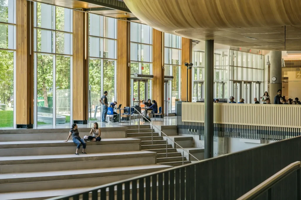 Shared spaces inside a large building, with wide seating steps and tables in a glazed timber atrium