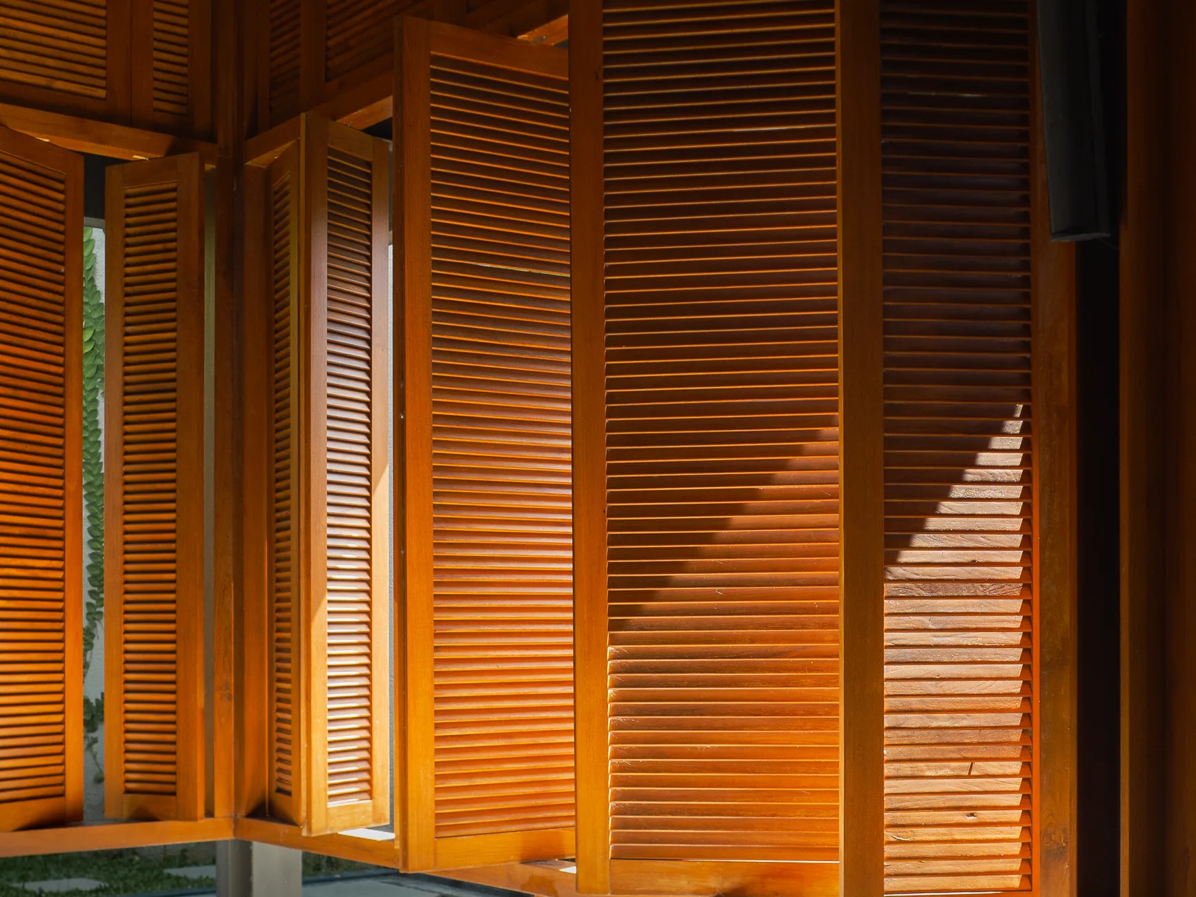 Folding timber louvred shutters glowing in low sunlight, casting striped shadows across the openings