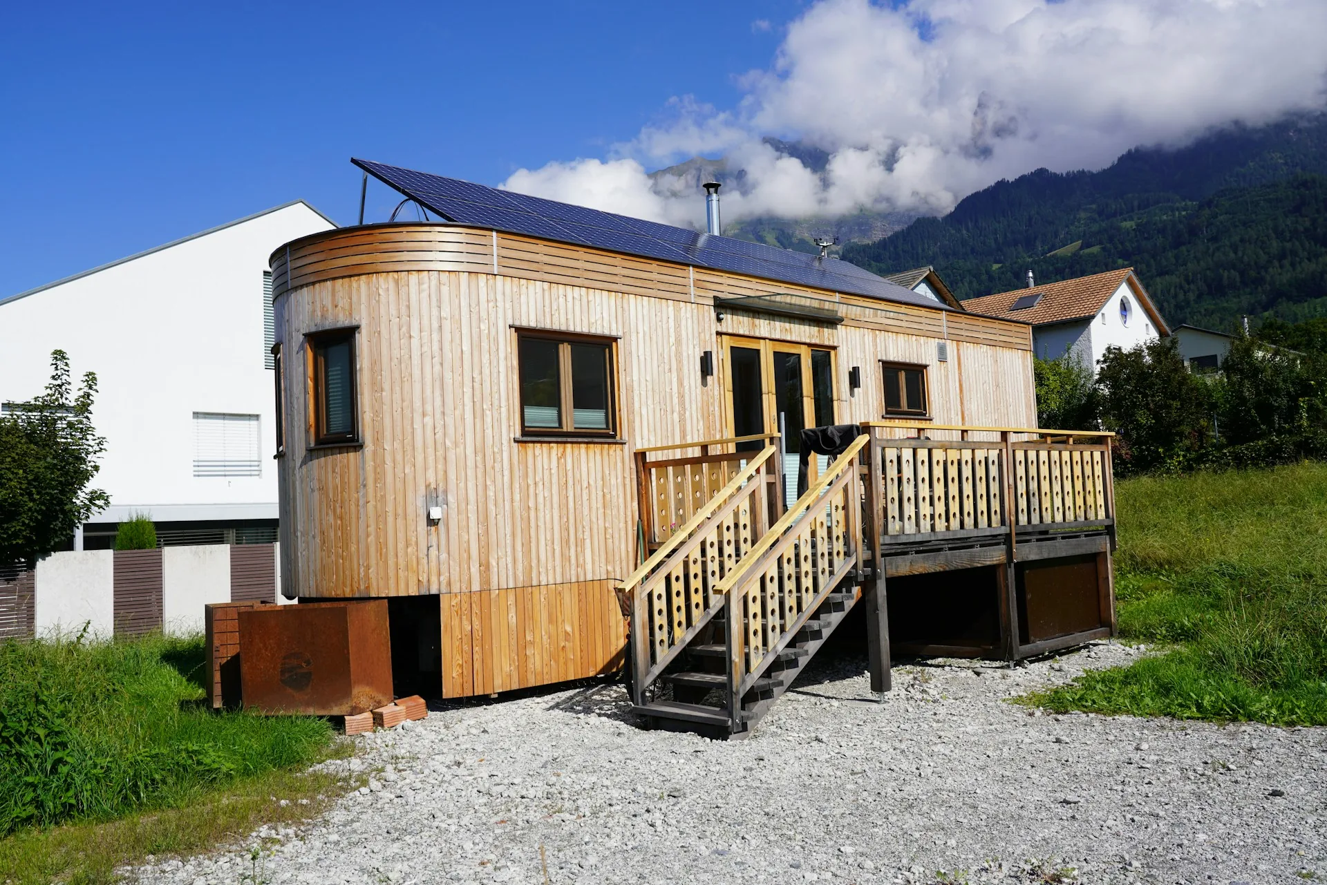 Modern timber-clad tiny house with a curved end wall, solar panels on the roof and a raised wooden deck