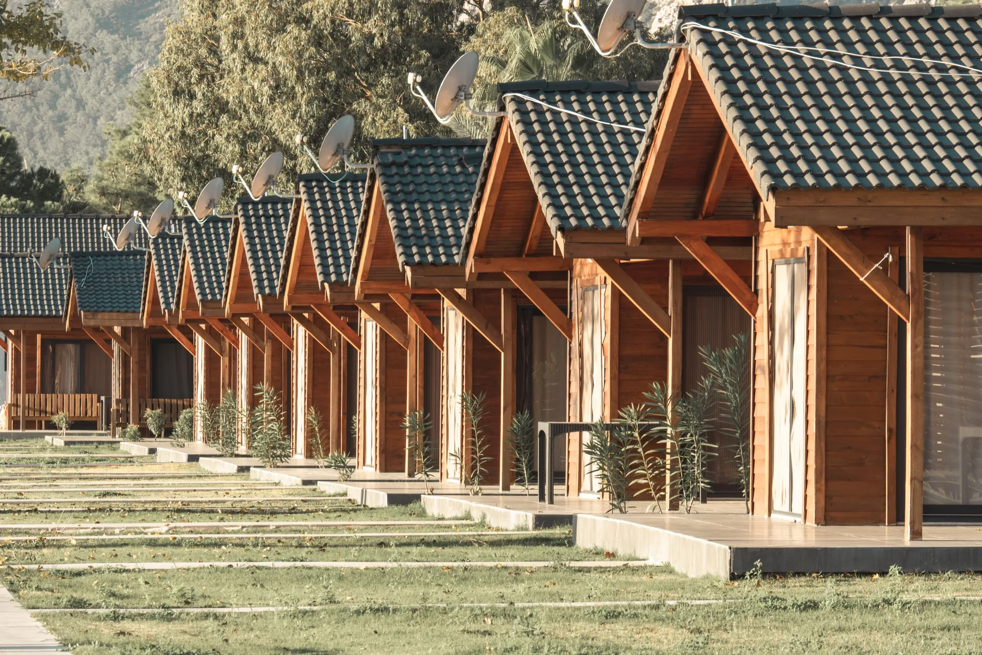 Row of identical small timber cabins with tiled gable roofs and front porches along a shared lawn