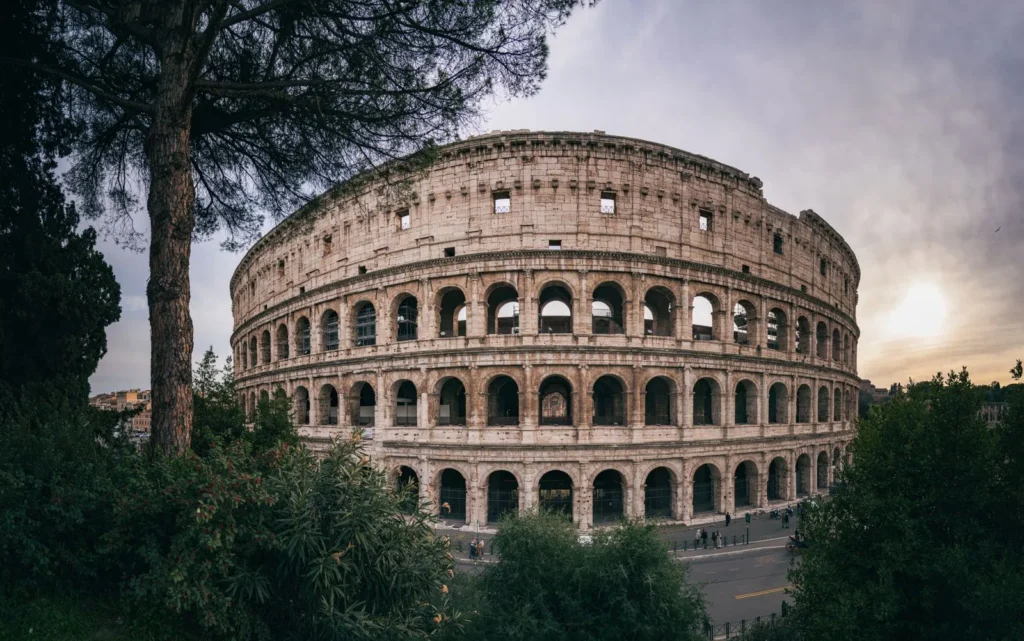 The Colosseum in Rome at sunset, its tiers of travertine arches framed by trees