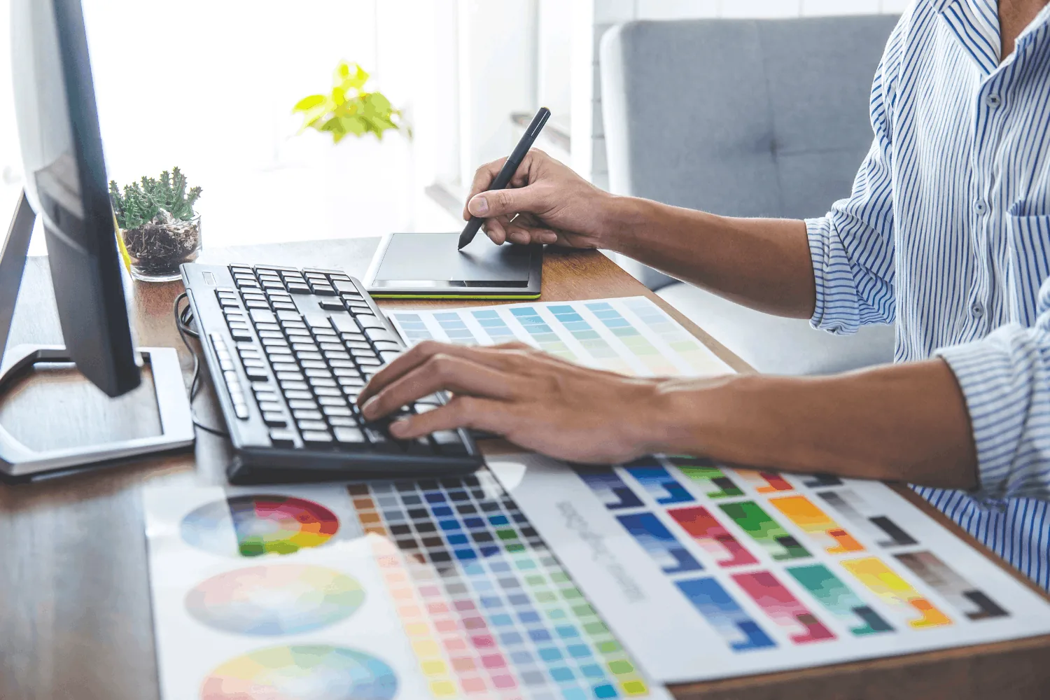 Designer working at a computer with a graphics tablet and keyboard over printed colour swatch charts