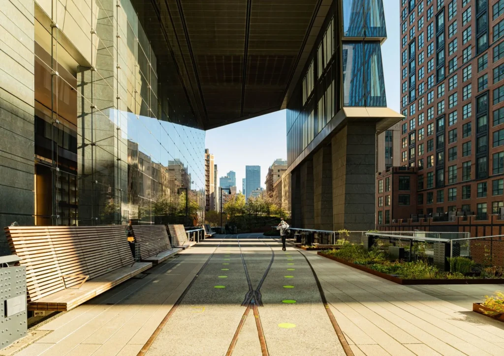 Timber benches and embedded rail tracks along the High Line walkway between Manhattan towers, one of the most inspiring public spaces