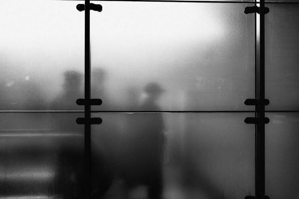 Blurred silhouettes of people moving behind frosted glass panels, showing translucency in architecture