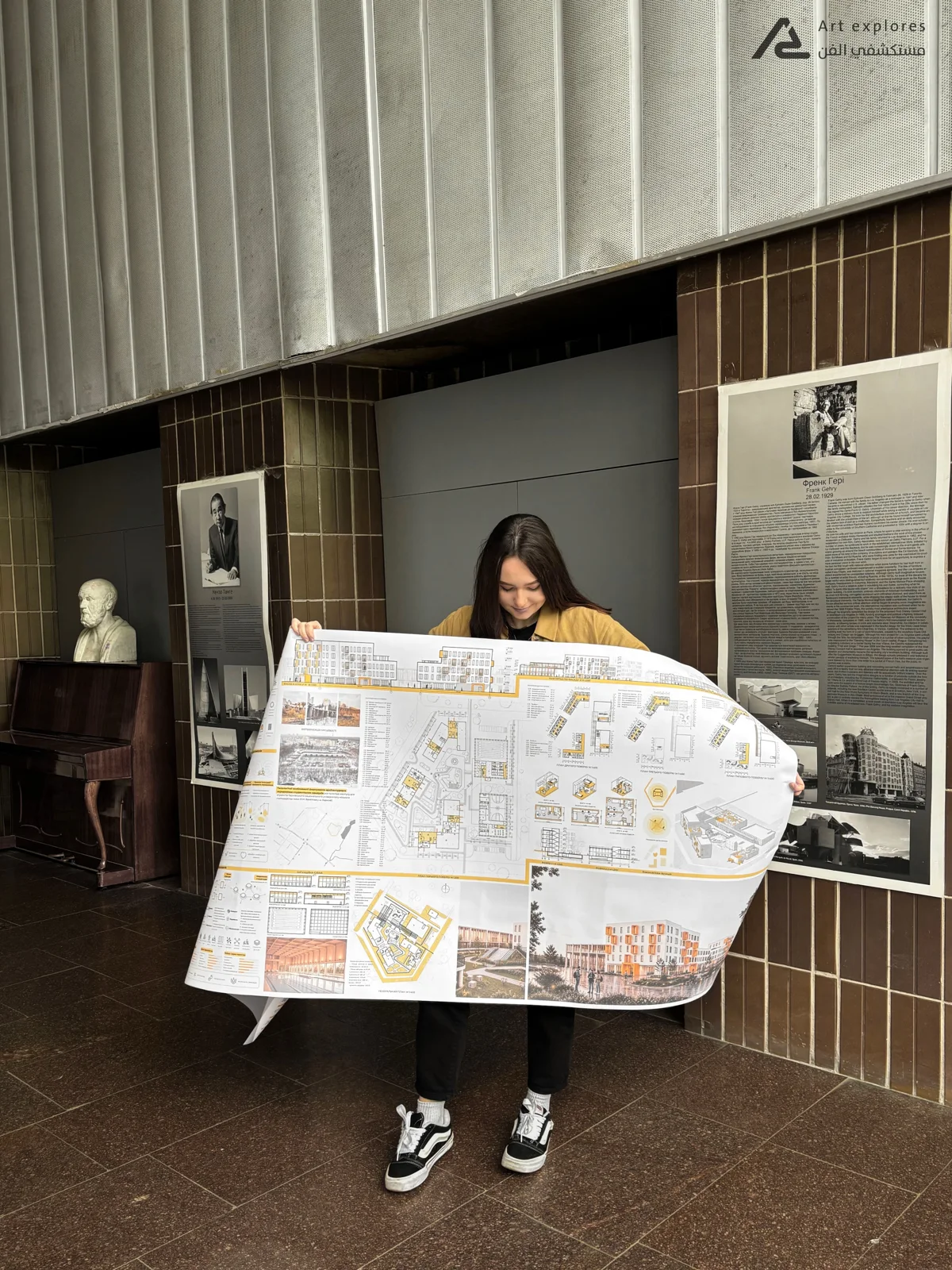 Photograph of a student holding a large printed presentation board in an exhibition hall