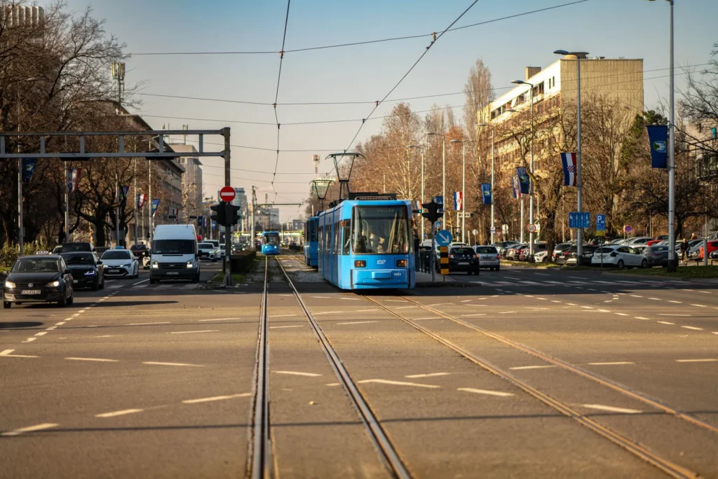 Blue tram running down a dedicated track in the middle of a wide city avenue in Zagreb