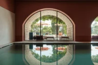 Indoor pool with terracotta walls and a stone arch whose glazed opening frames the garden and reflects in the water, Villa Argentina by 3LHD