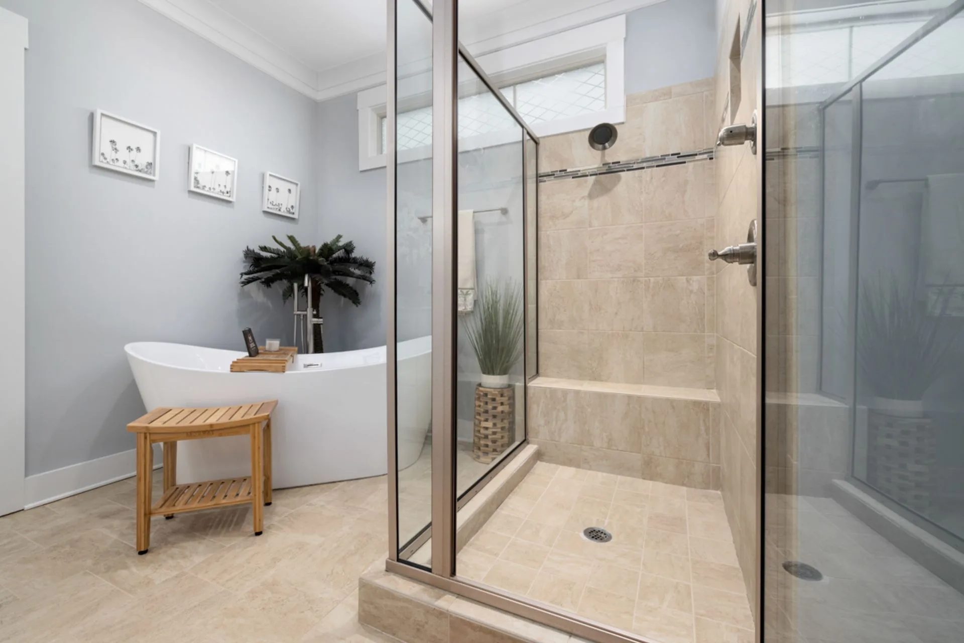 Bright bathroom with a walk-in glass shower beside a freestanding bathtub and a timber stool