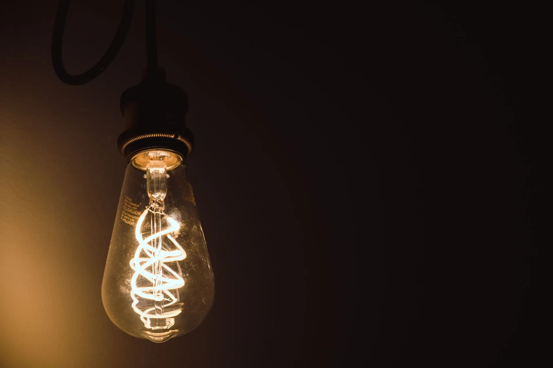 Warm glowing filament bulb hanging on a dark cord against a dark wall