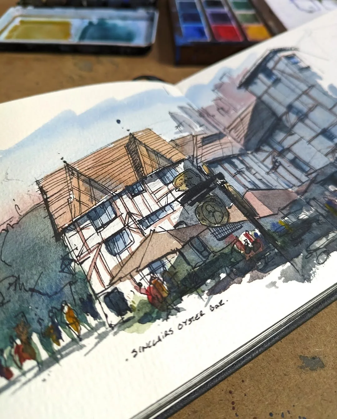 Watercolor and ink sketchbook drawing of a timber framed street building with pedestrians in the foreground