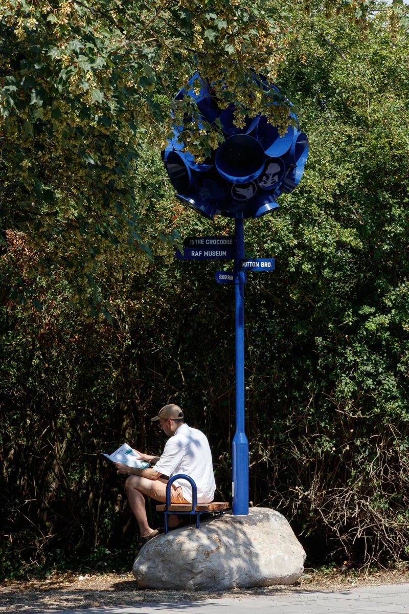 Dark blue sculptural lamppost on a boulder in a park with a person sitting on the base reading