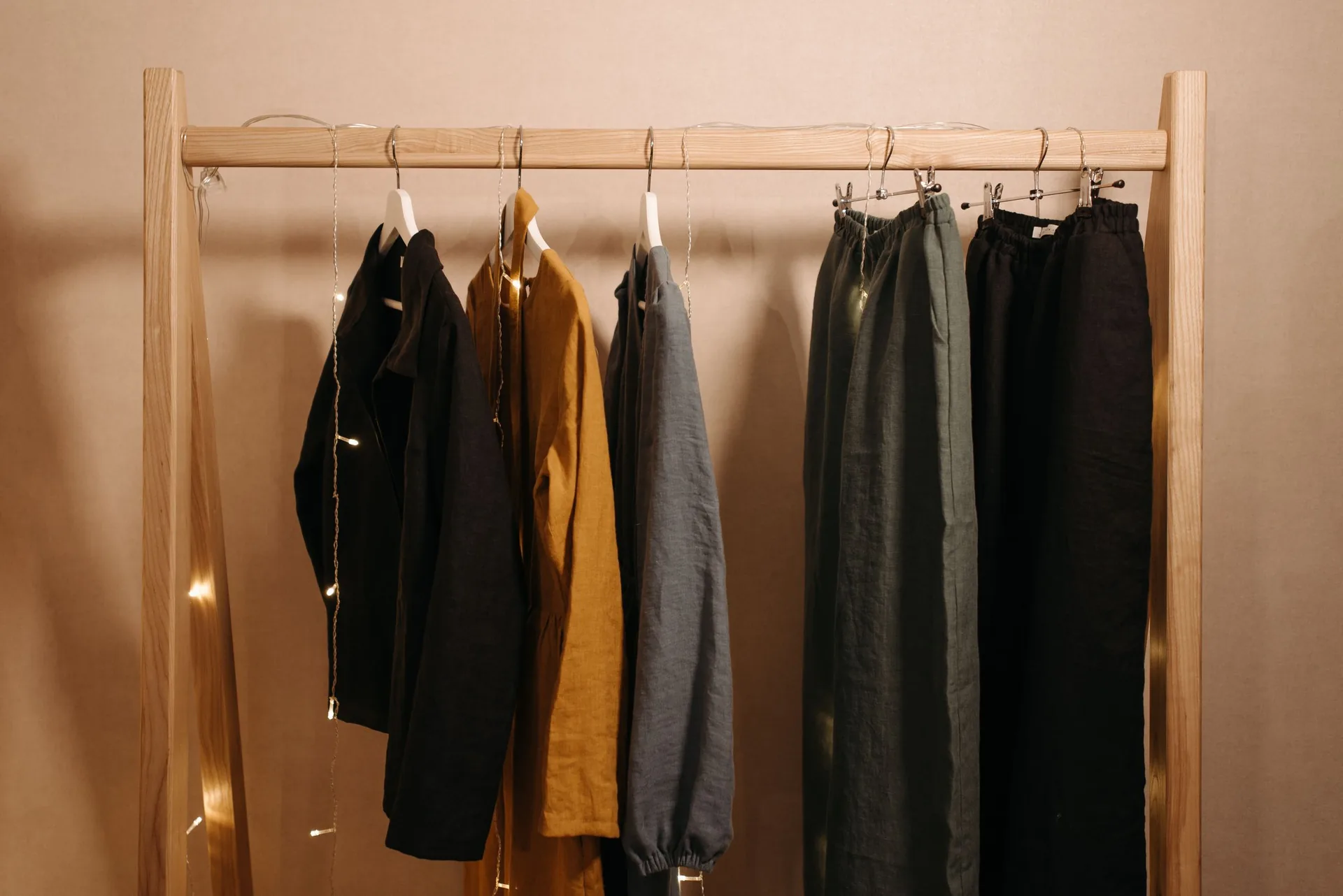 Wooden clothes rack with black, grey, olive and mustard jackets beside dark trousers, a small neutral capsule wardrobe