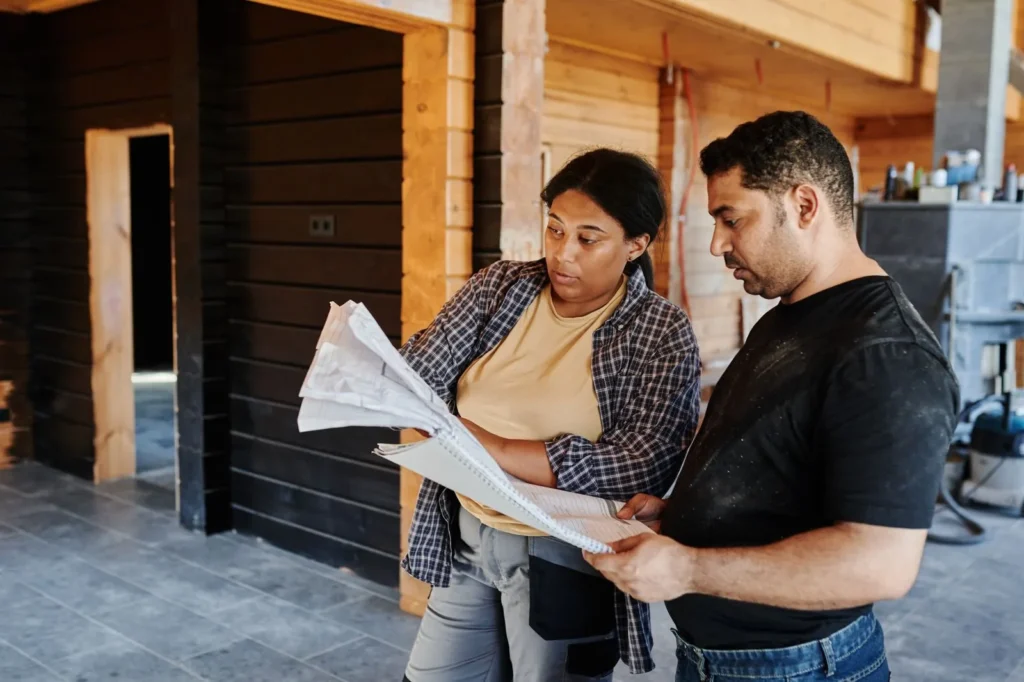 Client and builder reading through a printed document inside a timber house under construction, checking it against the architectural brief