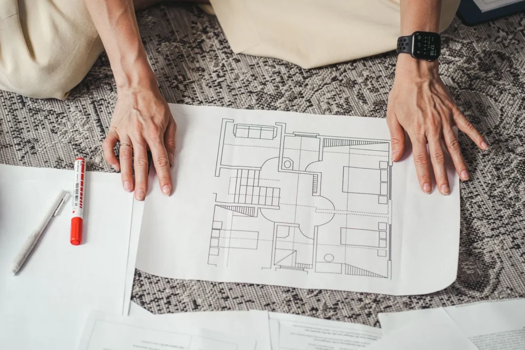 Hands resting on a printed apartment floor plan laid on a rug, with a marker and pen beside it