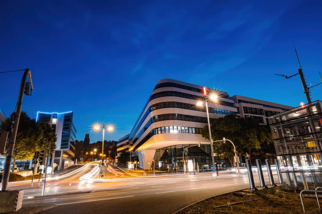 Curved office building at blue hour with lit windows and car light trails sweeping past