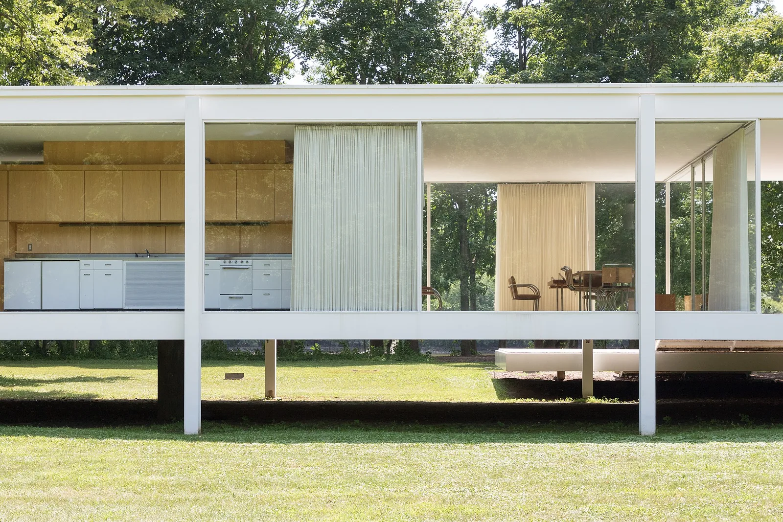 Farnsworth House by Mies van der Rohe, its floor to ceiling glass walls revealing the kitchen core and trees beyond