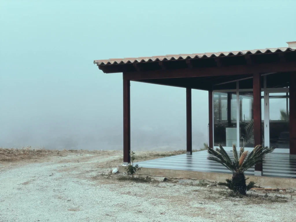 Modern house with a deep timber-roofed terrace standing in thick morning mist in Sicily
