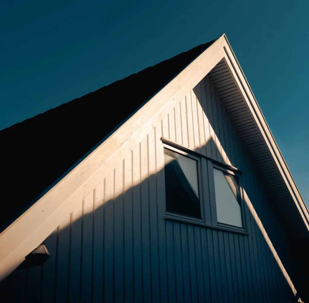 Sharp sunlight and shadow raking across the gable and window of a dark clad house