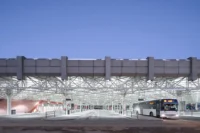 Bus platforms under the white steel space frame and concrete roof edge, with a bus at a stand at dusk, Zvonařka Bus Station by CH+K