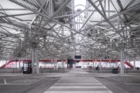 Pedestrian crossing through the platforms beneath the dense white steel roof lattice, the red wave in the distance, Zvonařka Bus Station by CH+K
