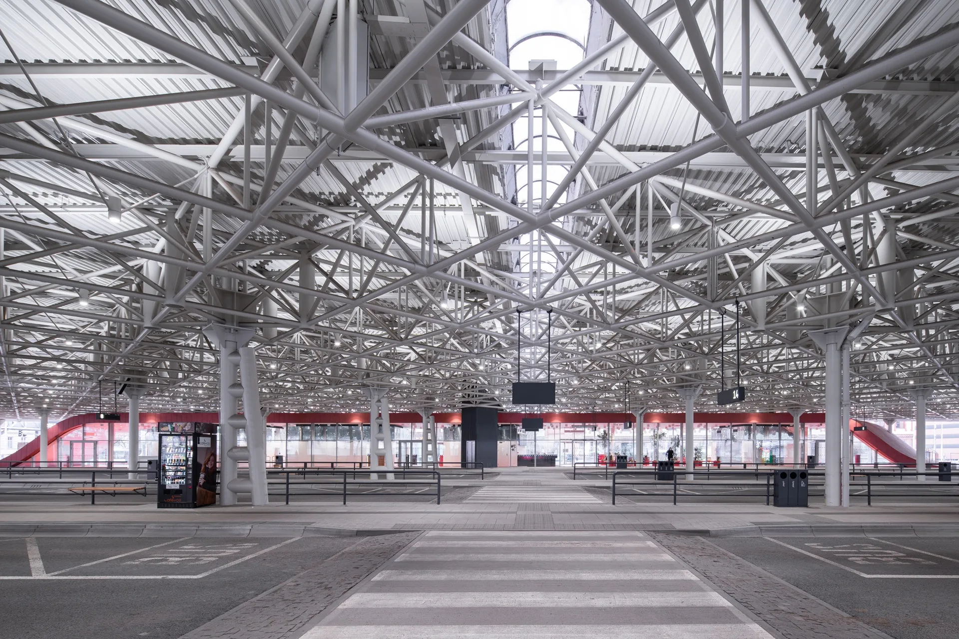 Pedestrian crossing through the platforms beneath the dense white steel roof lattice, the red wave in the distance, Zvonařka Bus Station by CH+K