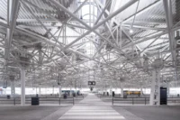 Rows of platforms and columns under the white steel space frame seen along a zebra crossing, Zvonařka Bus Station by CH+K