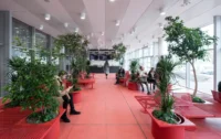 Red floored waiting room with red benches and large planters holding trees beside full-height glazing, Zvonařka Bus Station by CH+K