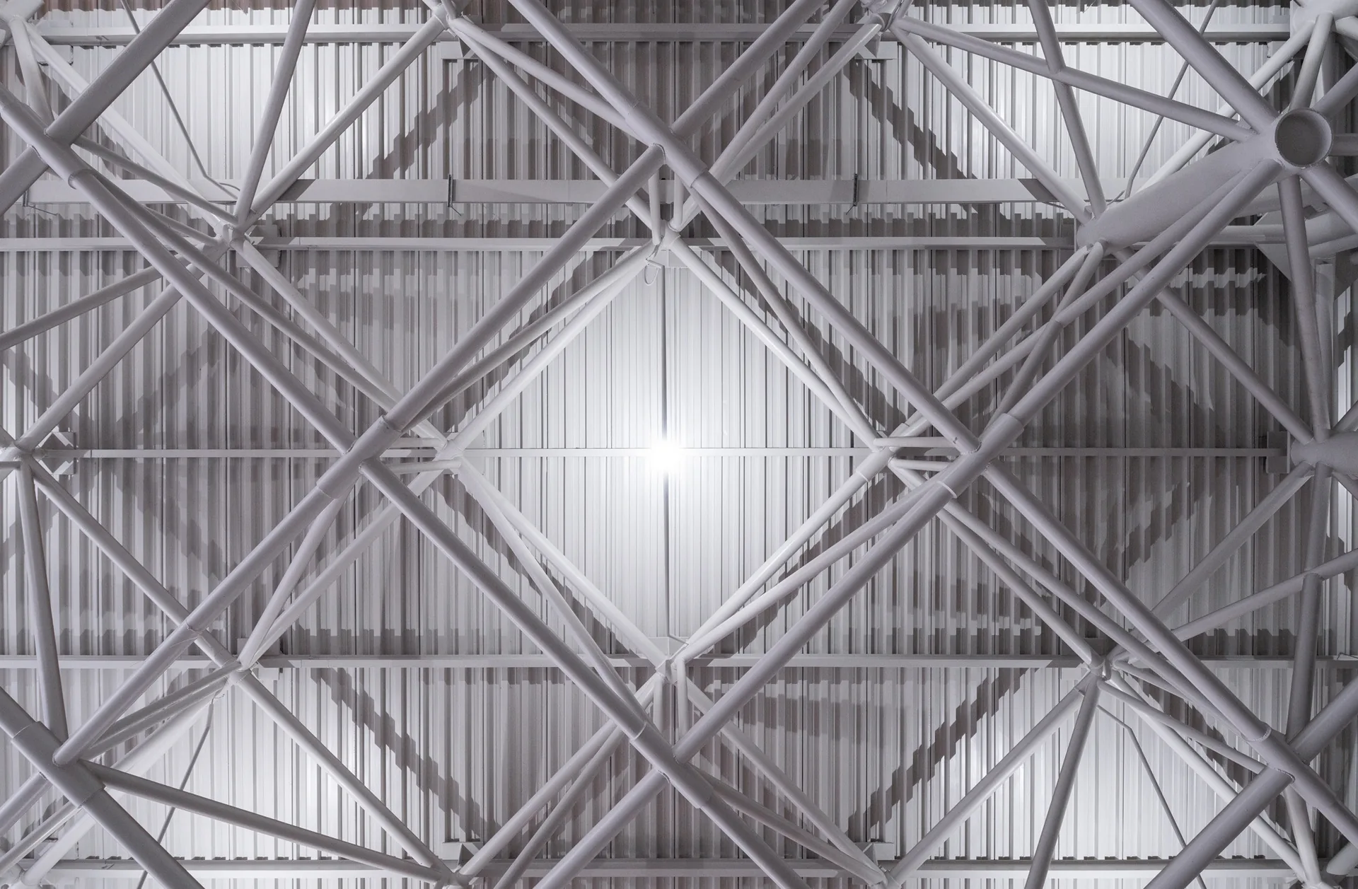 Close-up of the white tubular steel space frame beneath the corrugated roof deck, Zvonařka Bus Station by CH+K